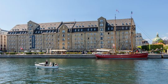 Hotel Admiral fra vandet med rød sejlbåd i forgrunden / Artelia / Rådgivende Ingeniører